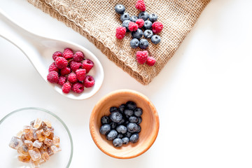 Making summer preserve. Raspberry, blueberry and sugar on white background top view copyspace