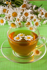 Herbal tea with fresh chamomile flowers on green wooden background