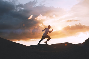 Athlete runs quickly through the hills outdoors at sunset
