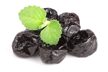 heap of dried plums or prunes with a mint leaf isolated on white background