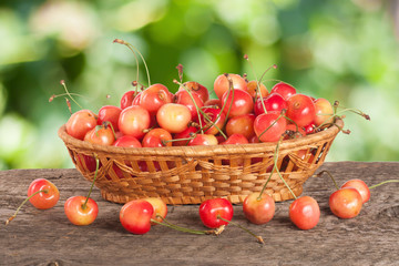 Yellow cherry in a wicker basket on a wooden table with a blurry garden background