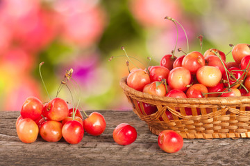 Yellow cherry in a wicker basket on a wooden table with a blurry garden background