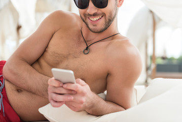 Cheerful youthful bearded man relaxing with mobile on resort