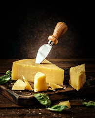 Parmesan cheese on wooden board with basil leaves. Pieces of cheese parmesan on wooden table and cheese knife. Vintage view.