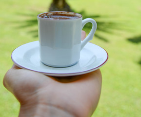 Close-up of male hand holding coffee to take away at early morning in park.