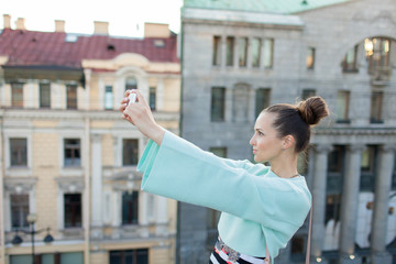 Cute sexy girl with brown hair stands on the roof of the house in the old town and makes a selfie on your smartphone