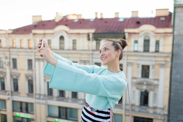 Cute sexy girl with brown hair stands on the roof of the house in the old town and makes a selfie on your smartphone
