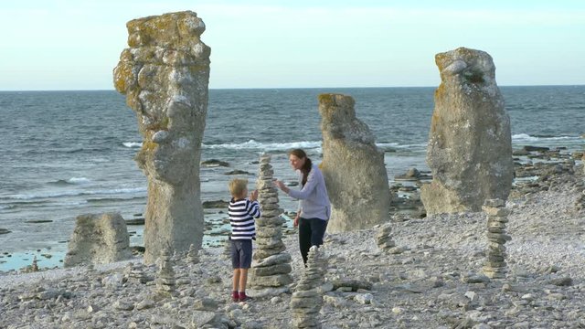 A boy and his mother building a stone stack by the rauk field Langhammars on the island Faro, Gotland, Sweden.