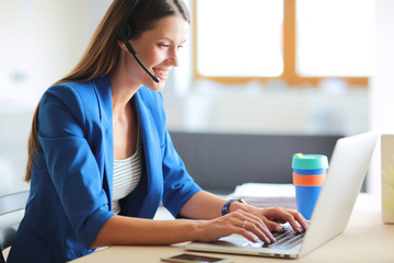 Portrait of beautiful business woman working at her desk with headset and laptop.