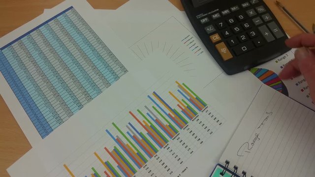 Accountant at his desk using a calculator and reviewing a spread sheet printout while taking notes