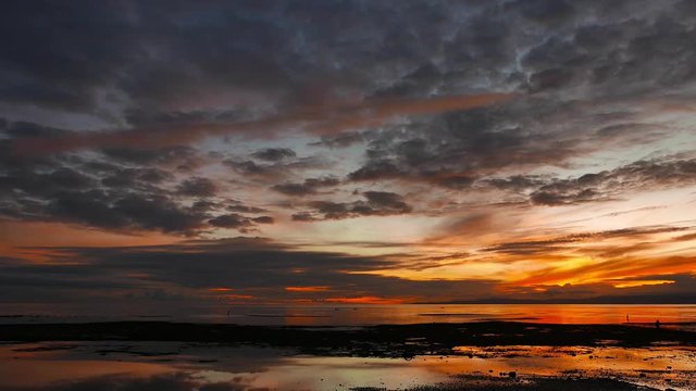An overcast, crimson colored sunrise video from Dumaguete City shores. Locals can be seen gathering shells from the shallow pools left behind by the low tide. Presented as real time.