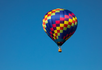 Teardrop shaped hot air balloon in rainbow colors in air with blue sky background