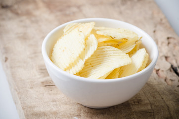 Potato chips in a bowl on wooden background