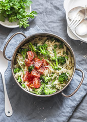 One pot orzo primavera. Orzo pasta with asparagus, broccoli, green peas and cream in a saucepan. On a light background, top view