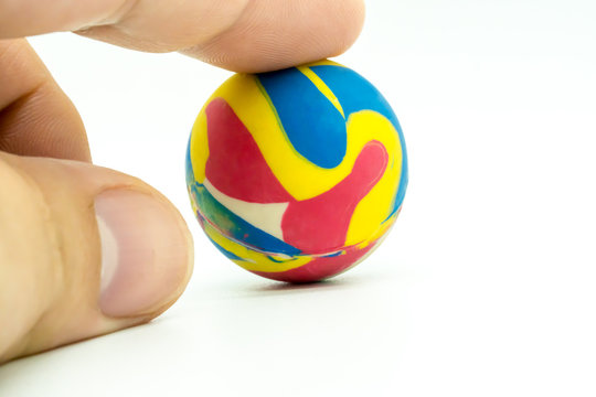 Index or pointing finger touching colorful rubber marble ball isolated on white