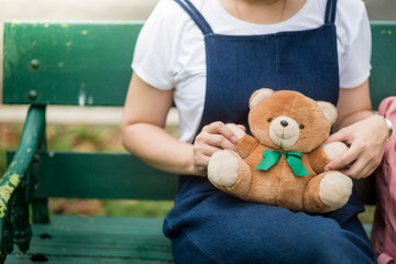 A girl play with bear doll sit on the green bench
