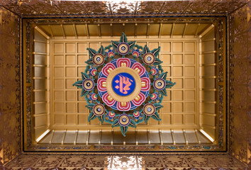 Om Sign with painted circular floral motif surrounding it. Mounted on a gold toned ceiling.