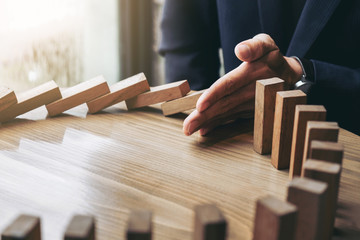 Close up of businessman hand Stopping Falling wooden Dominoes effect from continuous toppled or risk, strategy and successful intervention concept for business
