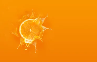 Fotobehang Schuif gesneden stuk oranje druppel op oranje achtergrond met sinaasappelsap spatwater met kopieerruimte © Kaikoro