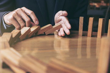 Close up of businessman hand Stopping Falling wooden Dominoes effect from continuous toppled or...