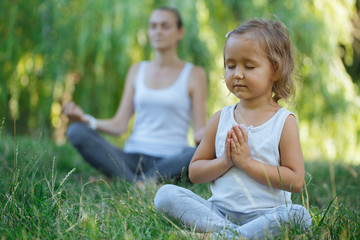 Young mother and cute little daughter meditating in lotus pose together