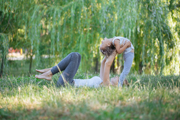 Mother and daughter doing yoga exercises on grass in the park at the day time.