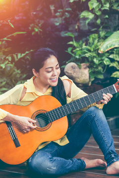  Asian woman playing acoustic guitar with bright sunlight. Vintage effect tone.