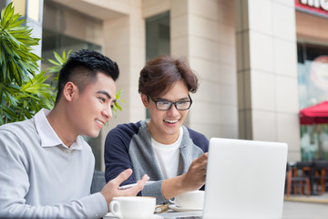 Two attractive mature students talking and working outdoors on laptop