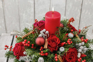 Christmas decoration with candle, red roses, fir, brunia and cinnamon sticks.