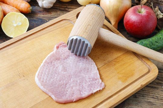 Meat mallet and beaten piece of veal on cutting board