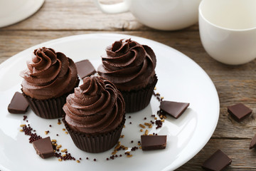Tasty cupcakes with pieces of chocolate in plate on wooden table