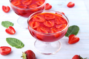 Jelly with strawberries in glass on white wooden table