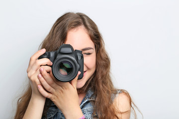 Portrait of young woman with camera on grey background