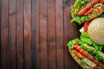 Hot dog and hamburger with cheese, meat and greens on Wooden background. Top view. Free space.