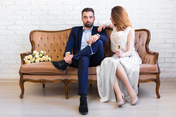 Obraz premium happy couple with glasses of champagne sitting on vintage sofa