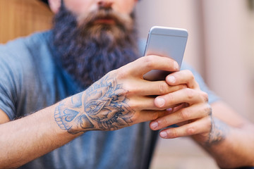 Bearded male in a hat holds a smartphone.