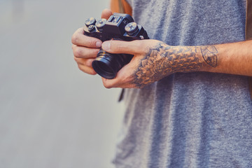 Fototapeta premium A man holds a compact film camera with tattooed arms.