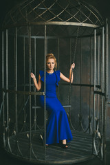 Fototapeta na wymiar Красивая девушка в вечернем длинном синем платье сидит на качелях в интерьерной студии