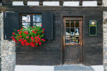 Fototapeta na wymiar Old wooden window with shutters and flowers near old wooden door and blackboard