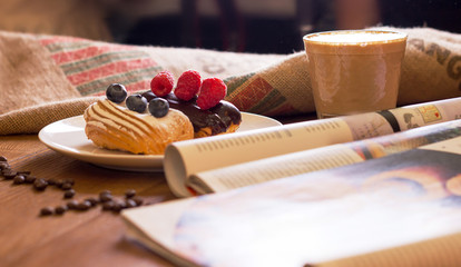 Cappuccino, cake with berries and a journa on table.