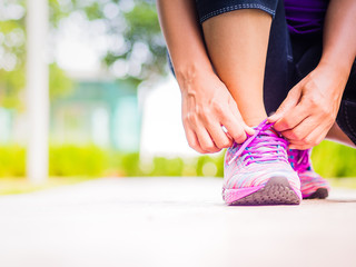 Running shoes - closeup of woman tying shoe laces. Female sport fitness runner getting ready for jogging in garden backgroound