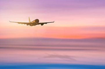 Airplane flying over blur tropical beach with smooth wave and sunset sky abstract background.