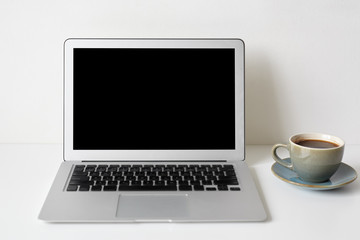 Modern technology, communication, electronic devices, gadgets, work and communication. Mock up of workplace: white table with coffee cup and generic notebook computer with blank copyspace screen