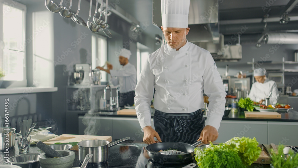 Wall mural famous restaurant chef fries fish on a hot pan. he works in a modern kitchen.