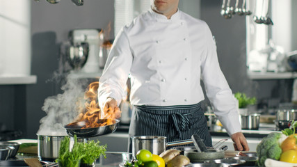 Professional Chef Fires up Oil on a Pan. Flambe Style Cooking. He Works in a Modern Kitchen with Lots of Ingredients Lying Around.