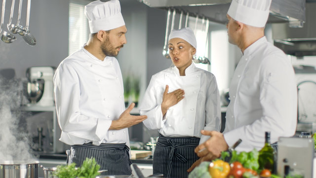 In the Modern Kitchen Team of Cooks Have Discussion. Kitchen is Full of Food Ingredients, Vegetables, Meat, Boiling Soup.