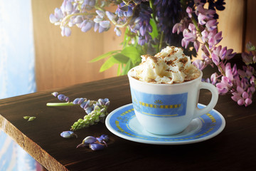 Morning coffee. Coffee cappuccino in white with a blue cup, on a table, next to a bouquet of flowers