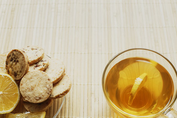 Glass cup of tea with biscuits and lemon on a light wooden background.Cup of tea with lemon and biscuits