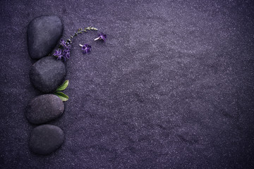 the black stone with green leaf and small cute purple flower decoration on stone plate background with copy space for spa and meditation concept background