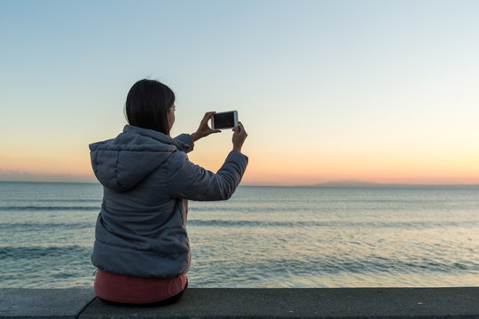 Woman taking photon with seascape and sunset